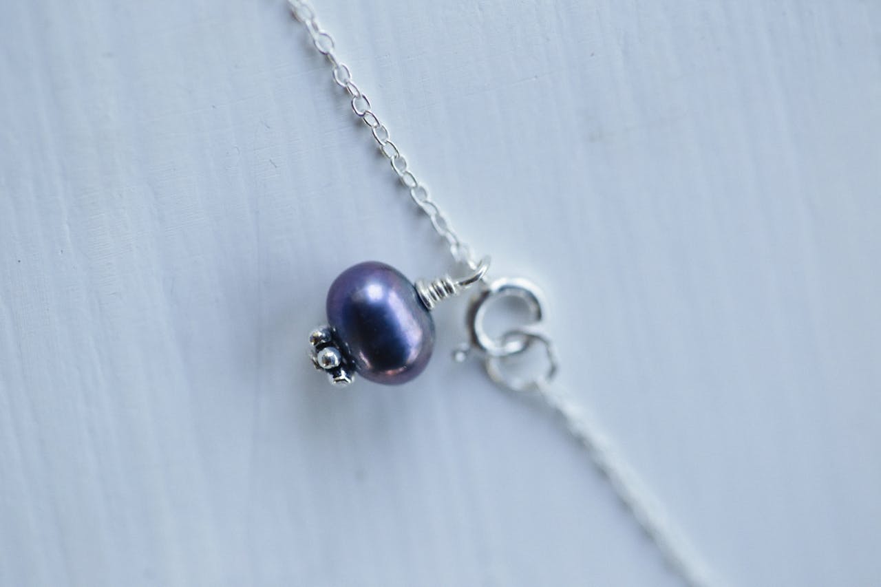 Close-up of a silver necklace with a purple pearl pendant, showcasing fine details.